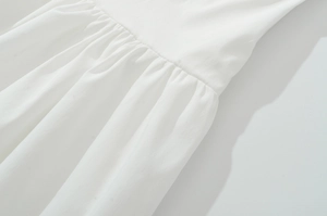Detailed close-up of white dress showing elegant waist pleats and cotton linen texture