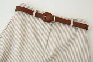 Détail d'un pantalon rayé beige et blanc avec ceinture à boucle ronde en similicuir marron