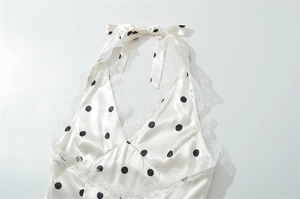 Nahaufnahme eines weißen Polka-Dot-Satin-Oberteils mit Spitzenbesatz und Schleife am Hals