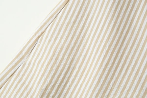 Détail du tissu en coton à rayures beige et blanc avec coutures précises sur l'ourlet