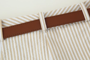 Détail de la taille en seersucker rayé avec fine ceinture en cuir marron sur le pantalon