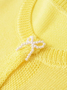 Macro shot of delicate white pearl bow applique on a lemon yellow fine knit sweater