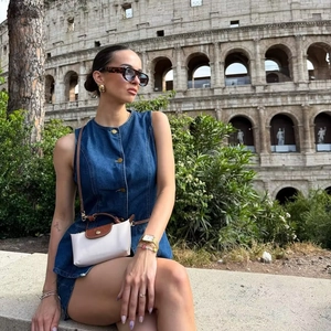 Sleeveless denim vest dress with round neck buttons shown in front of the Colosseum