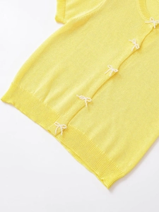 Detailed view of yellow knit cardigan featuring delicate white beaded pearl bows
