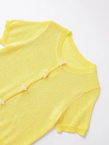 Detail of yellow short-sleeve knit cardigan featuring delicate white beaded bow buttons