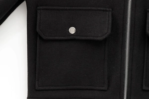 Detailed macro view of a black wool jacket featuring a silver metal zipper and pocket flap