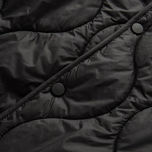 Macro shot of wavy quilted black jacket fabric with matte black metal snap buttons