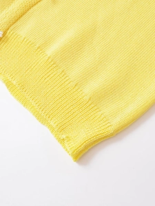 Close-up of yellow knit sweater texture featuring a delicate white pearl button detail