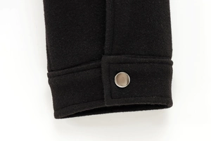 Detailed macro view of black wool jacket cuff with polished silver metal snap button