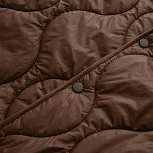 Detail of dark brown quilted jacket showing wave stitching pattern and matte black snap button