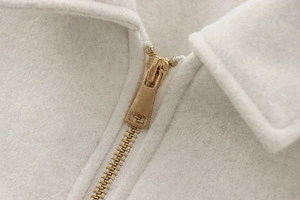 Detail of premium gold metal zipper and soft white wool texture on a stylish jacket