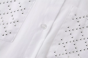 Close-up of white cotton shirt featuring silver metal studs on front pocket details