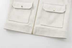 Close-up of beige textured fabric jacket featuring gold zipper and metal buckle pockets