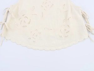 Detail of off-white sleeveless top with floral embroidery and side bow ribbons