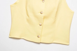 Detailed close-up of pale yellow linen sleeveless vest with marble textured buttons