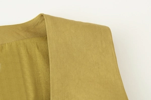 Dettaglio del tessuto satinato e cuciture curate sulla spalla della camicia senape