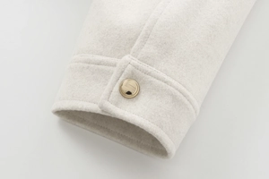 Detailed close-up of wool jacket cuff with decorative gold button and textured fabric