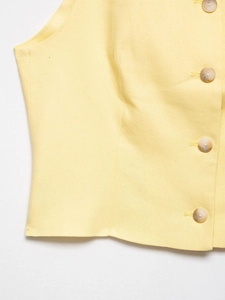 Detail of light yellow linen vest showing textured fabric and marble-patterned buttons