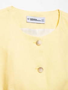 Detail of light yellow cotton linen vest showing round neck and marble texture buttons