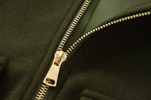 Detailed close-up of premium gold metal zipper on dark green wool-textured jacket