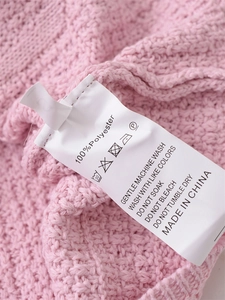 Detail of white washing label on soft pink knitted sweater made of 100% polyester fabric
