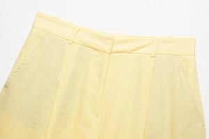 Detail of light yellow linen trousers showing waistband loops, pleats, and side pockets