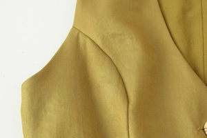 Dettaglio macro del tessuto strutturato giallo senape con cuciture e bottone in metallo dorato