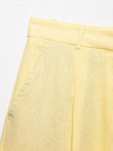 Detailed close-up of light yellow linen trousers showing belt loops and pocket stitching