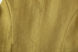 Vista macro della trama del lino giallo oliva e dettagli cuciture sul blazer donna