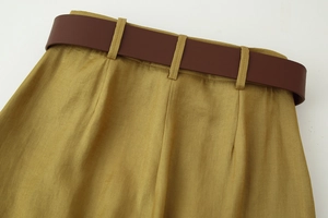 Dettaglio dei pantaloni in raso giallo senape a vita alta con cintura in ecopelle marrone