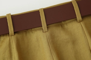 Dettaglio dei pantaloni in raso giallo senape con trama tessuta e una cintura in pelle marrone