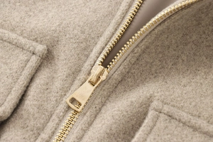 Detail of premium golden metal zipper on oatmeal wool blend jacket with fuzzy texture