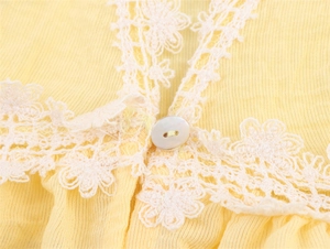 Detailed close-up of yellow textured fabric with white floral lace trim and pearl button