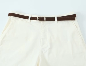 Detail view of cream tailored shorts featuring a slim dark brown belt and silver buckle