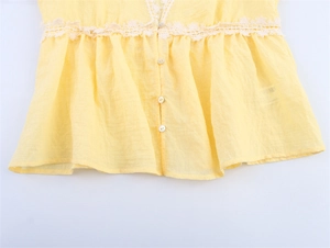 Detail of pale yellow sleeveless top featuring white lace trim and ruffled hem detail