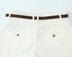 Detail of white shorts with brown branded belt and amber buttons on rear pockets