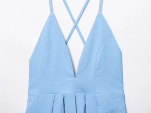 Detail of light blue dress showing deep V-neck, crisscross straps, and pleated texture