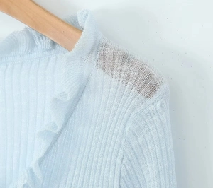 Detailed macro view of delicate light blue knit cardigan with ruffle trim details