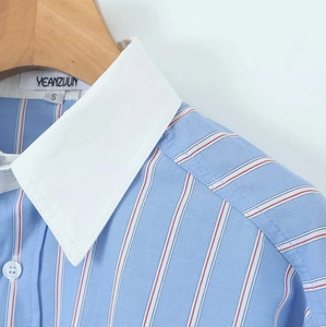 Détail d'une chemise à rayures bleues et blanches avec col blanc sur cintre en bois