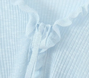 Close-up of light blue ribbed knit cardigan with ruffled collar and tie-up detail