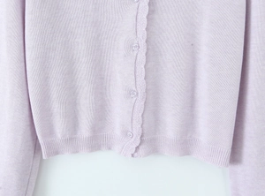 Macro detail of lavender knit cardigan featuring scallop trim edges and clear buttons