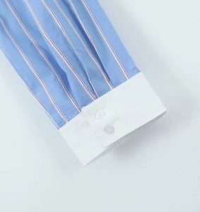 Détail du poignet d'une chemise rayée bleue et blanche avec tissu contrasté et deux boutons