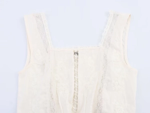 Detail view of a white lace sleeveless top with floral embroidery and wavy scalloped edges