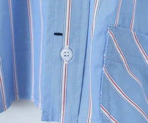 Détail d'une chemise à rayures bleu clair avec bouton blanc et surpiqûre de poche