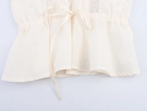 Detailed close-up of delicate lace trim and ribbon bow on a white elegant camisole top