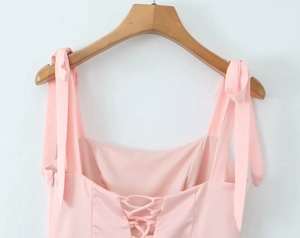Close-up of pink summer dress with shoulder bow ties and lace-up corset back detail