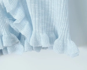 Close-up of light blue knit cardigan showing vertical rib texture and ruffled edge details