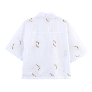Détail de la chemise blanche avec broderie florale délicate et texture ajourée élégante