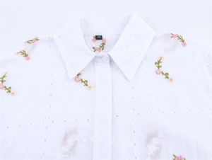 Détail d'une chemise en coton blanc avec broderie florale rose et texture de tissu ajouré