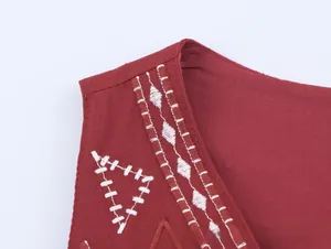 Vue macro d'une broderie géométrique blanche sur un gilet en lin rouge foncé